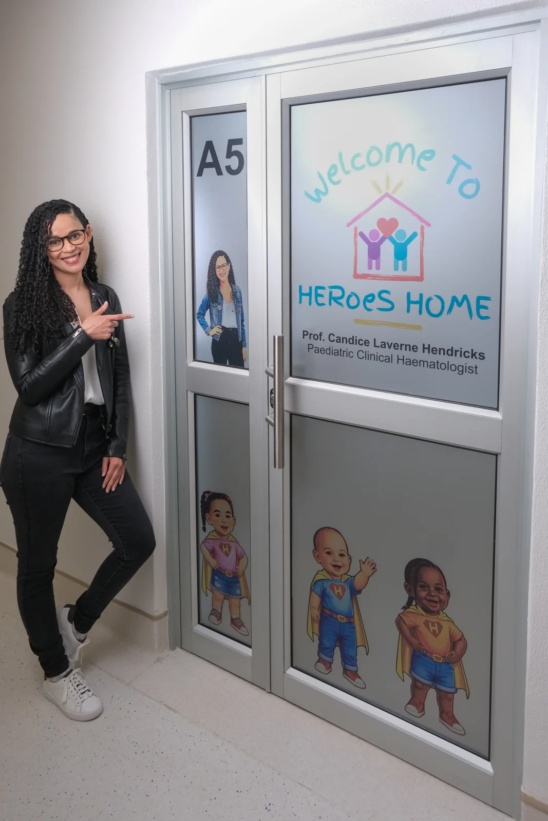 Prof. Candice Hendricks pointing to the HERoeS HOME Suite A5 entrance
