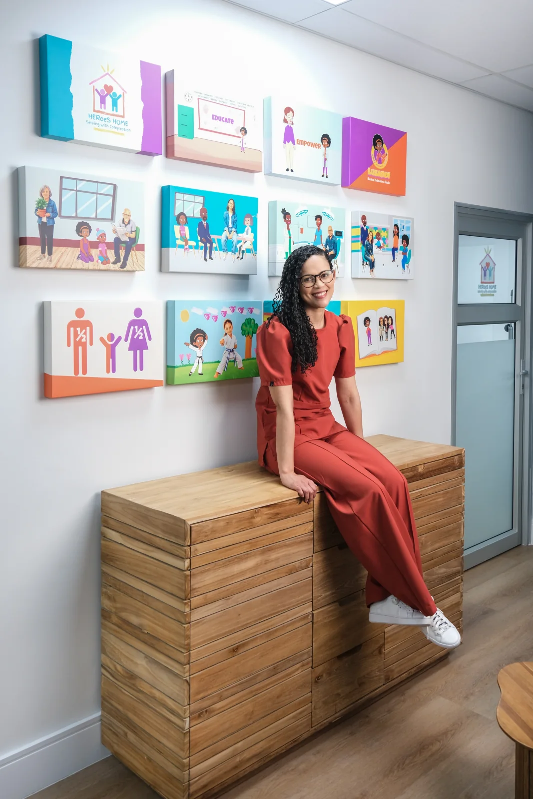 HERoeS HOME team member in coral scrubs seated beneath colourful practice artwork