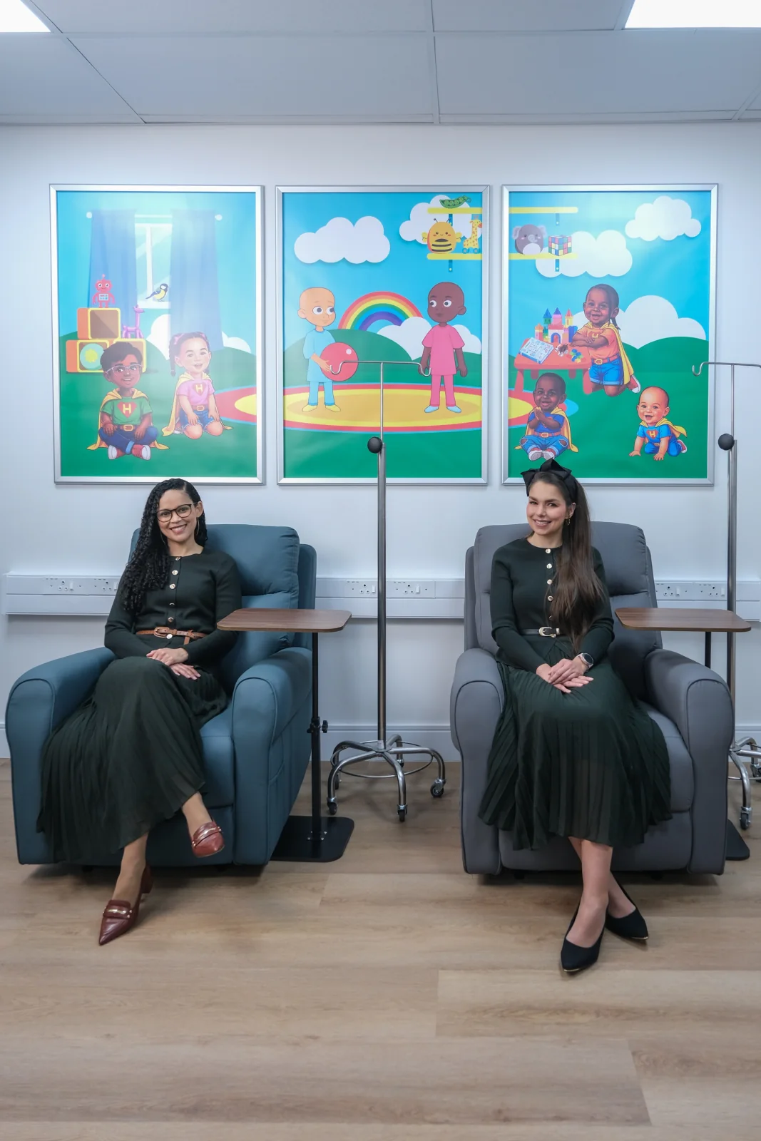 Two HERoeS HOME team members seated beneath colourful children’s artwork